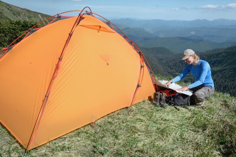 Touristes de randonnée pointant la carte dans les montagnes assis près de la tente sur la falaise. Voyageuse solo en week-end. Survivre dans la nature, se reposer à l'extérieur, mener une vie saine