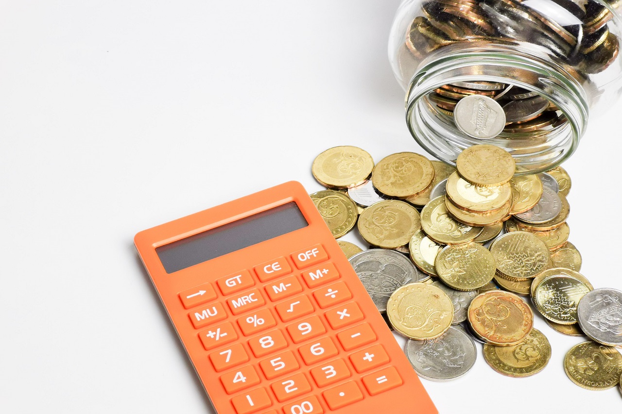 Une calculatrice avec une pile de pièces et un pot transparent rempli de pièces placés à côté sur fond blanc, symbolisant la planification financière