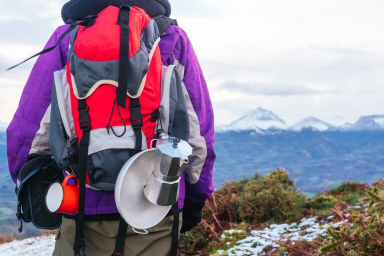 sac à dos rouge avec des ustensiles de camping en arrière-plan un paysage de montagnes enneigées.